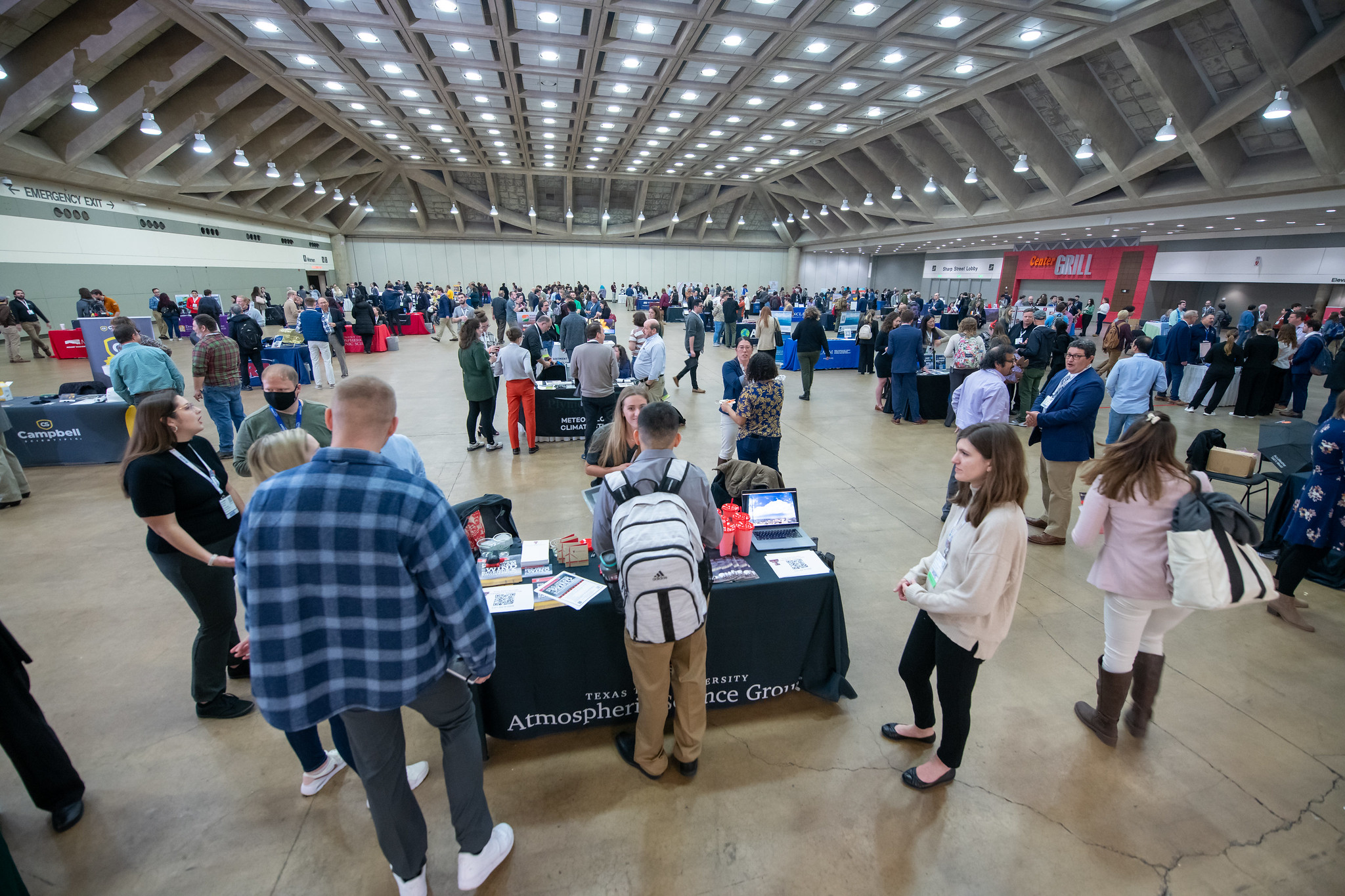 A large indoor career fair with people standing around various tables. Tables are covered with informational materials.