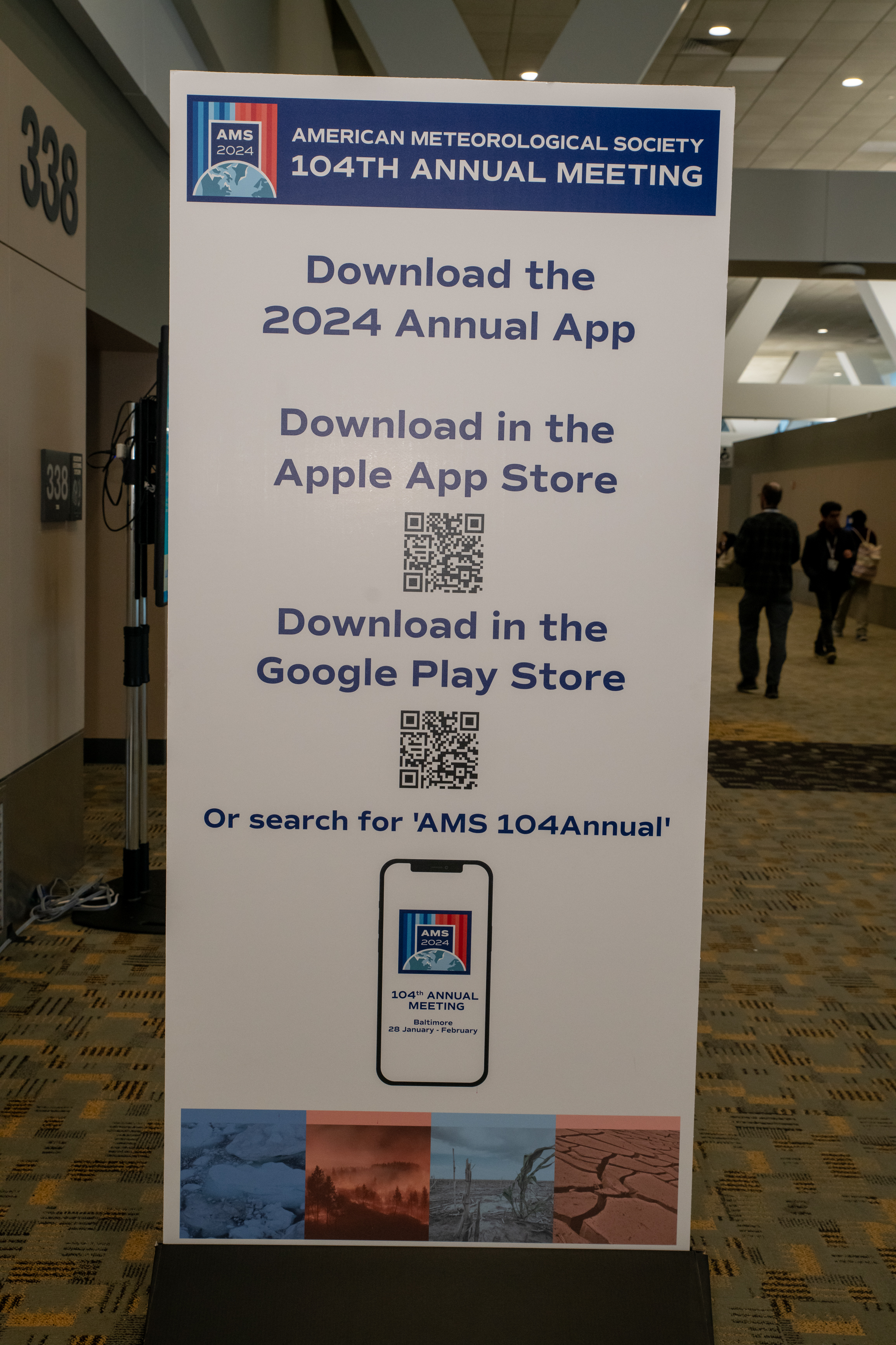 Sign for the American Meteorological Society 104th Annual Meeting promotes its 2024 app, QR codes, app stores, and a hallway setting.