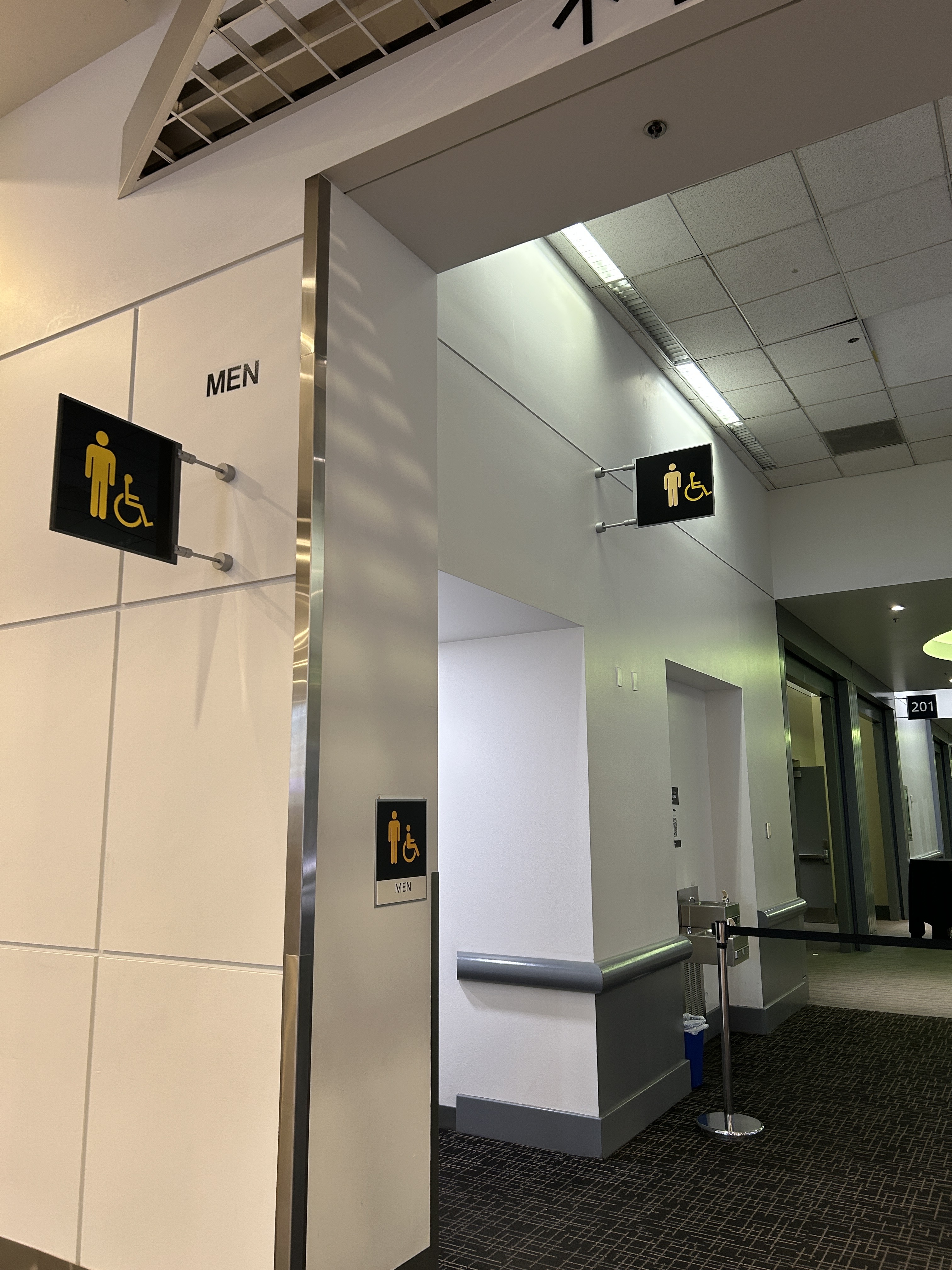 Modern hallway with multiple black MEN restroom signs featuring wheelchair-accessibility symbols; bright, clean interior with a quiet tone.