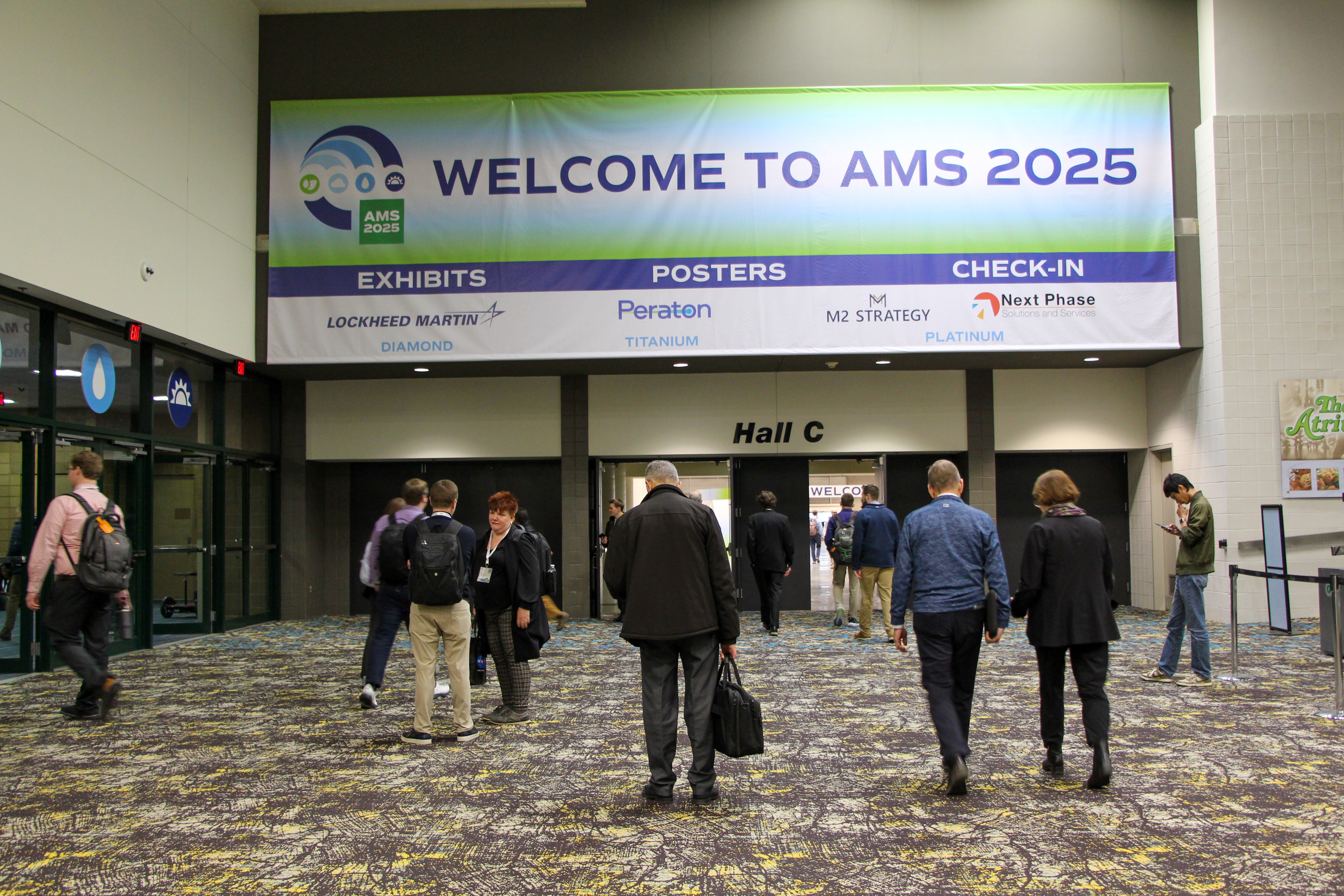 Attendees enter Hall C beneath a “Welcome to AMS 2025” conference banner, creating a busy, professional atmosphere in the lobby.